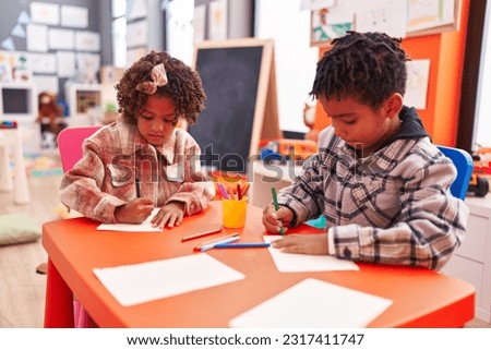 Adorable african american boy and girl preschool students sitting on table drawing on paper at kindergarten Royalty-Free Stock Photo #2317411747