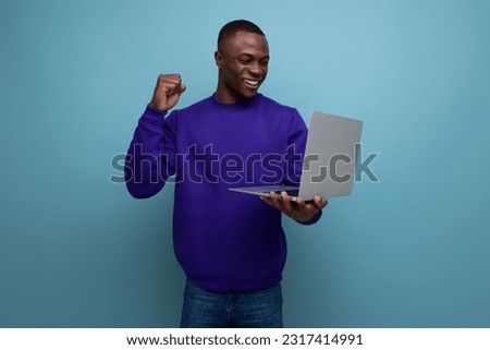 30s dark-skinned American man dressed in a blue sweater works remotely with a laptop