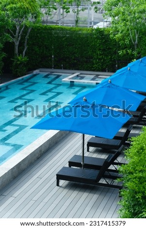 ฺBed and blue umbrella near Large modern swimming pool in luxury hotel.