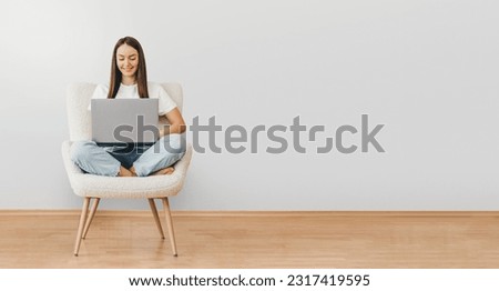 portrait of caucasian woman holding laptop computer while sitting on a chair isolated over gray background. web banner. copy space