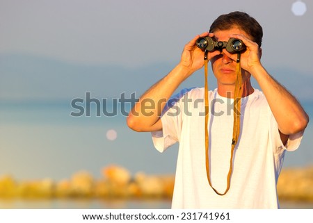 Looking through binoculars ; Man with binoculars on the shore watching the ships at sea