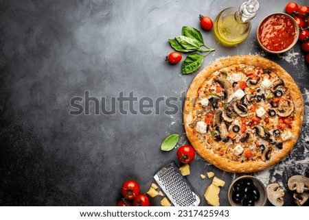 Tasty vegetable pizza and cooking ingredients tomatoes and basil on black background. Top view