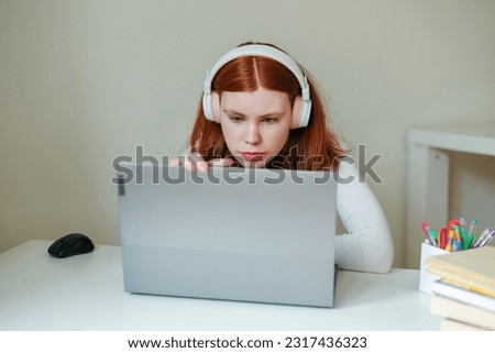 A young woman in headphones sits at home in front of a laptop and records a podcast, blog, growth and development training.