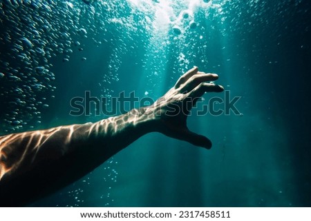 male hand underwater in the dark view under splashes and bubbles with sun rays