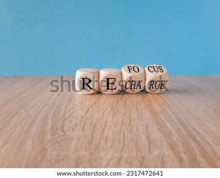 Refocus and recharge symbol. Businessman turns cubes and changes the word 'refocus' to 'recharge'. Beautiful wooden table, blue background. Business refocus and recharge concept. Copy space.