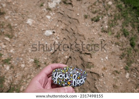 Dirt bike imprint on dirt trail with kindness rock held over