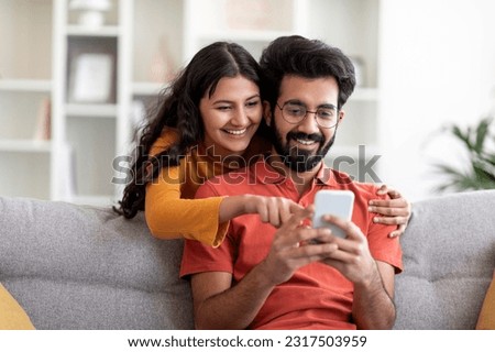 Mobile Gaming. Cheerful Indian Couple Playing Online Games On Smartphone At Home, Young Happy Eastern Spouses Having Fun With Mobile Phone While Relaxing On Couch In Living Room, Free Space Royalty-Free Stock Photo #2317503959