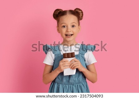 Portrait Of Cute Little Girl With Chocolate Bar In Hands Looking At Camera, Happy Preteen Female Kid Enjoying Sweet Dessert, Cheerful Child Posing Over Pink Background In Studio, Copy Space Royalty-Free Stock Photo #2317504093