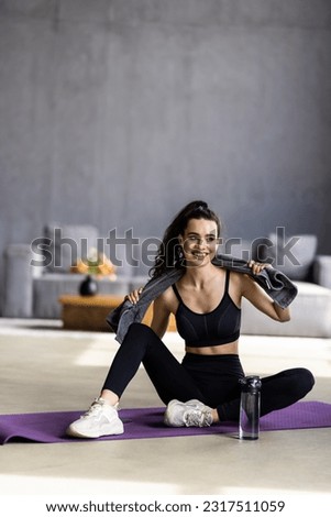 Satisfied fitness blogger resting after workout at home with water, woman take break on mat at domestic gym. Healthy lifestyle, body care, aqua balance and remote lesson