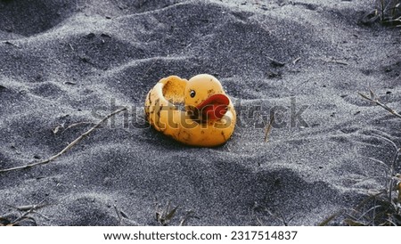 Close-up to a rubber yellow toy duck left on the sand by the beach. A symbol of swimming, childhood, friendship, fun game.