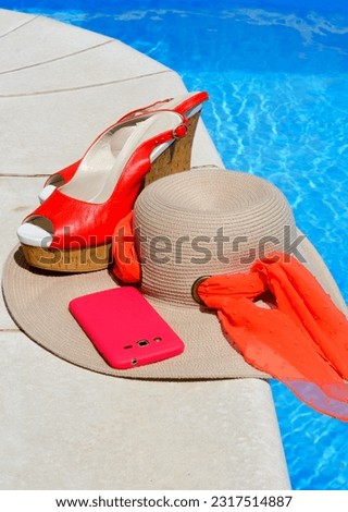 Women's hat, sandals and mobile phone next to the pool. Red beautiful sandals and panama on a background of blue water.