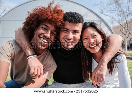 Portrait of a group of teenage students smiling and bonding at university campus. Three multiracial friends hugging and posing with friendly expression. Diverse cheerful peeople having fun together