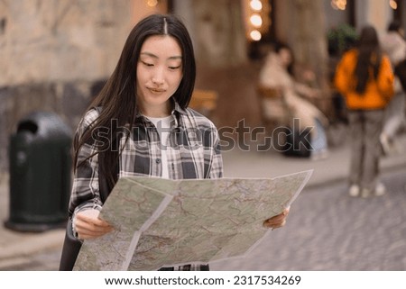 Portrait of a beautiful brunette Korean woman holding a map on the streets of the old city. Asian woman tourist or business lady traveling in Europe.