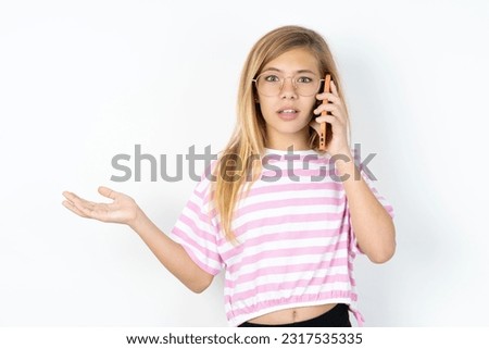 Happy beautiful caucasian teen girl wearing striped T-shirt over white wall sending a message on his smartphone or taking a selfie  and making ok sign with his hand.