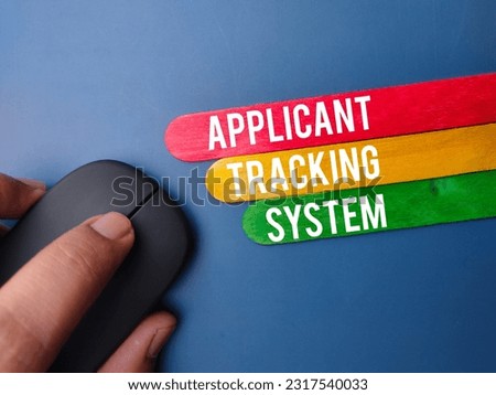 Wireless mouse and wooden stick with the word APPLICANT TRACKING SYSTEM on blue background Royalty-Free Stock Photo #2317540033