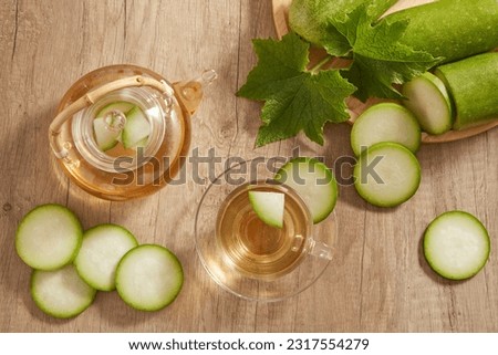 On a wooden table, a transparent teapot and cup filled with winter melon tea displayed with a tray of fresh winter melon. Winter melon (Benincasa hispida) is good for health Royalty-Free Stock Photo #2317554279