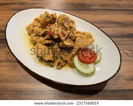 This is a picture of a dish called Salted Egg Chicken. It’s a crispy chicken cooked with salted egg sauce with a little bit of chili and spring onions. Served with slices of tomato and cucumber.