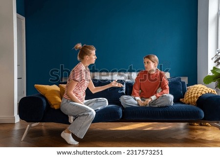 Upset mother arguing with child sitting on sofa in living room. Difficulties in raising teenage daughter. Parent scolds teen for bad behavior. Misunderstanding between children and parents Royalty-Free Stock Photo #2317573251