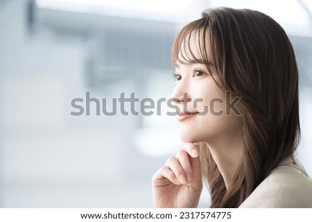 A young Japanese woman in a suit staring into the distance with a smile. An image of suits working in an office, changing jobs or finding employment. Royalty-Free Stock Photo #2317574775