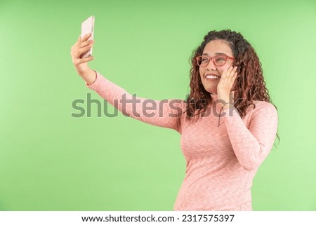 Excited young woman making a video call with her cell phone, on a green background