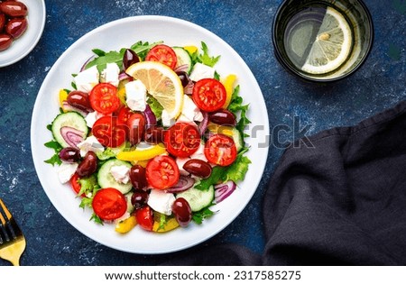Tasty Greek salad with feta cheese, kalamata olives, tomatoes, paprika, cucumber and onion, healthy mediterranean food. Blue table background, top view