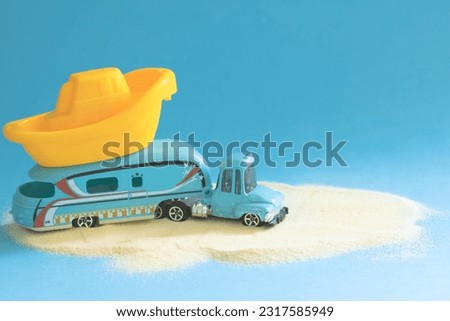 Toy retro caravan car with a plastic boat on a blue background. Concept of family summer vacation and travel by trailer. Minimalistic summer retro composition with children's toys. Close-up