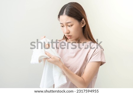 Housewife, asian young maid woman hand in holding white T-shirt, looking at cloth stain, spot dirty or smudge on clothes, dirt stains for cleaning before washing, making household working at home. Royalty-Free Stock Photo #2317594955
