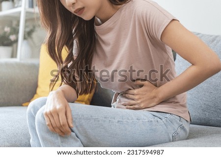 Flatulence asian young woman intolerance hand in stomach ache, suffer from food poisoning, abdominal pain and colon problem, gastritis or diarrhoea when at home. Patient belly, abdomen or inflammation Royalty-Free Stock Photo #2317594987