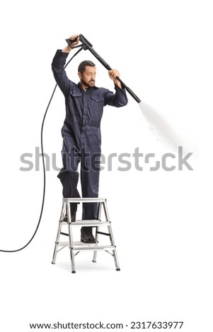 Man in a uniform using a pressure washer and standing on a ladder isolated on white background Royalty-Free Stock Photo #2317633977