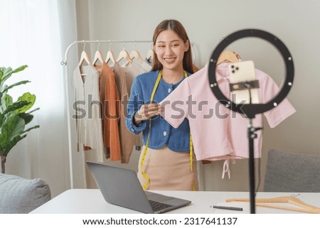 social media market concept. Young Asian woman seller showing second-hand clothes during live streaming in the mobile application.