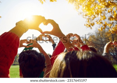 Group of friends making heart shapes with their hands against sunset. Young people walking in park in autumn time. Volunteers expressing love outside, nature protection Royalty-Free Stock Photo #2317645197