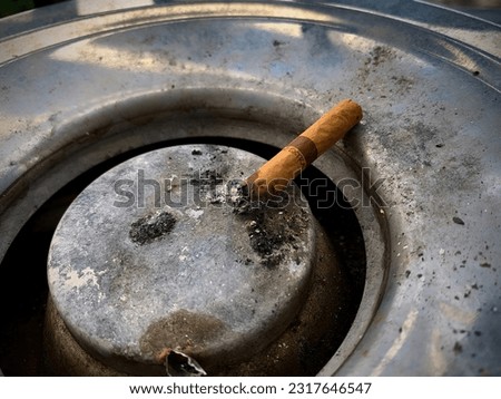 Used cigarette on ash-covered ashtray highlighting smoking and social issues.