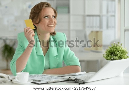 Young beautiful businesswoman sitting at table with laptop and holding small shopping cart