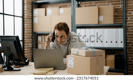 Middle age hispanic woman ecommerce business worker talking on the smartphone using laptop at storehouse office