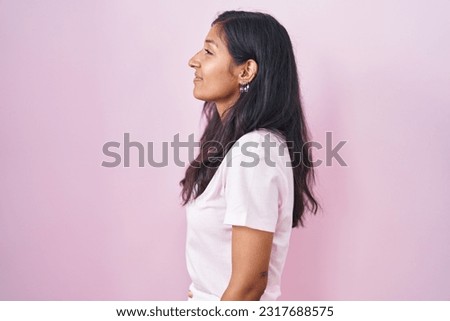 Young hispanic woman standing over pink background looking to side, relax profile pose with natural face and confident smile.  Royalty-Free Stock Photo #2317688575