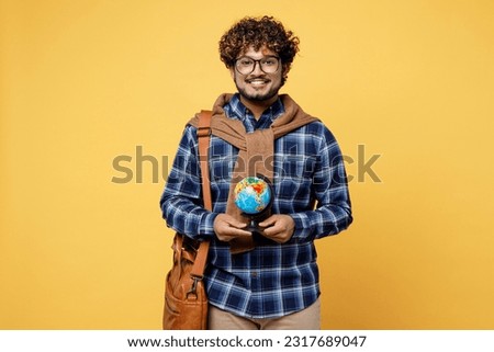 Young smiling happy teen Indian boy IT student he wear casual clothes shirt glasses bag hold in hand globe Earth map isolated on plain yellow color background High school university college concept