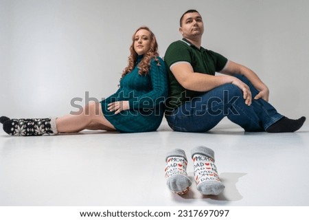 young pretty pregnant girl and man sitting on a light background, isolated. Creating and waiting for a young firefighter family