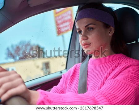 A girl in a pink sweater and a sports headband driving a right-hand drive car, following all the road rules with a flickering red danger sign in the window Royalty-Free Stock Photo #2317698547