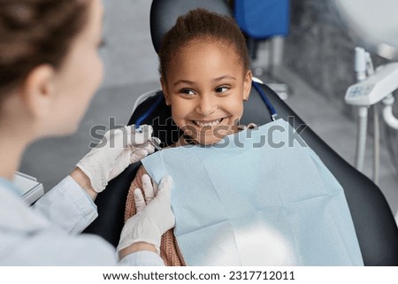 Portrait of smiling little girl in dental chair with nurse preparing her for teeth check up, copy space Royalty-Free Stock Photo #2317712011