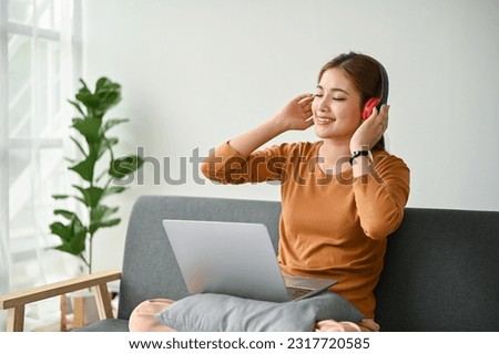 A happy and relaxed Asian woman enjoys listening to music through her headphones on sofa at home. Leisure and lifestyle concepts
