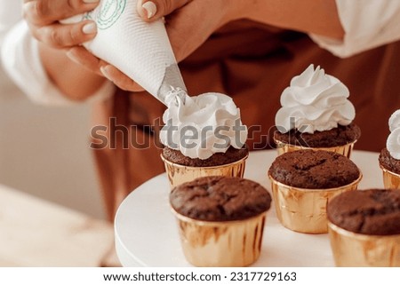 Pastry chef in the kitchen decorates chocolate cupcakes with cream close-up Royalty-Free Stock Photo #2317729163