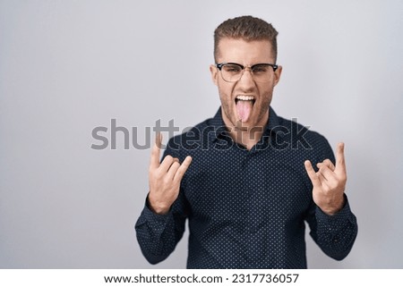 Young caucasian man standing over isolated background shouting with crazy expression doing rock symbol with hands up. music star. heavy concept. 