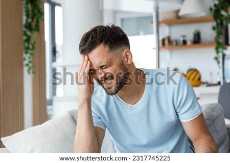 Closeup of young man suffering from headache at home, touching his temples, copy space, blurred background. Migraine, headache, stress, tension problem, hangover concept