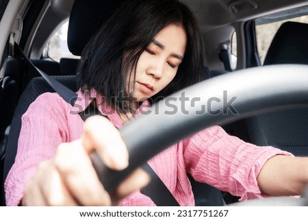 Sleepy and Fatigued Asian Woman Falls Asleep while Driving, the Danger of Drowsy Driving, unsafe driving behavior concept  Royalty-Free Stock Photo #2317751267