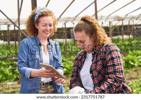 Happy female farmer sharing tablet PC with coworker at farm