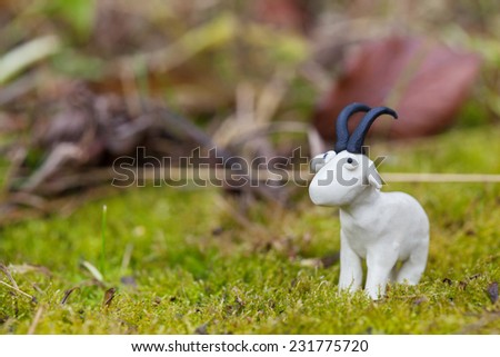 Plasticine world - little homemade white goat on green background, selective focus and place for text