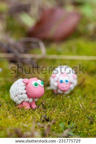 Plasticine world - little homemade white sheep with blue and green eyes on green background, selective focus on left one and place for text