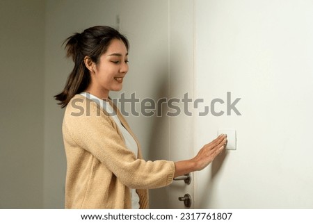 Earth Hour. Asian beautiful woman turn off or on the light to saving electrical energy. Finger pushing light switch turn on or off. White switch Royalty-Free Stock Photo #2317761807