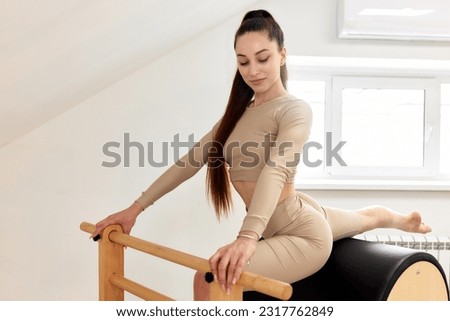 A young girl is doing Pilates on the barrel ladder reformer. A slim brunette in a beige bodysuit does exercises to strengthen and stretch her muscles. Fitness concept, special fitness equipment.