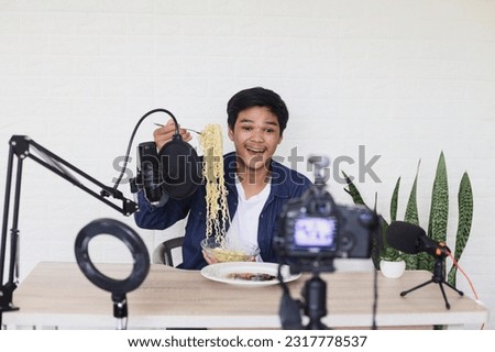 Asian man food blogger showing noodle to camera while creating new food content video for his channel by using smartphone. Food review blogger. Royalty-Free Stock Photo #2317778537